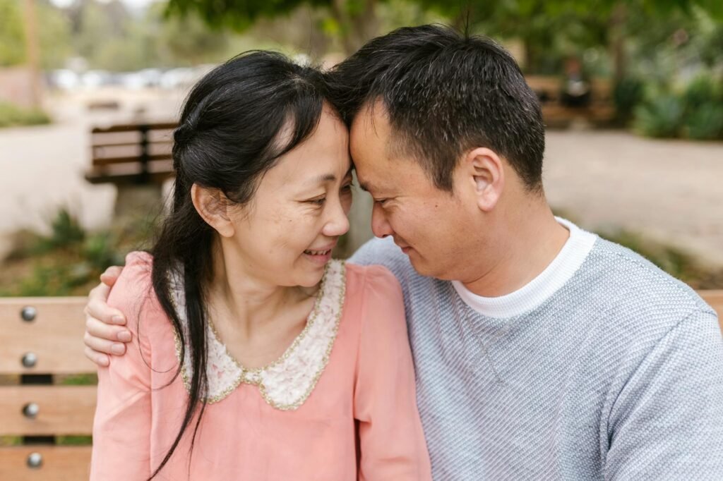 Smiling Asian couple embracing on a sunny day outdoors, sharing a moment of joy.
